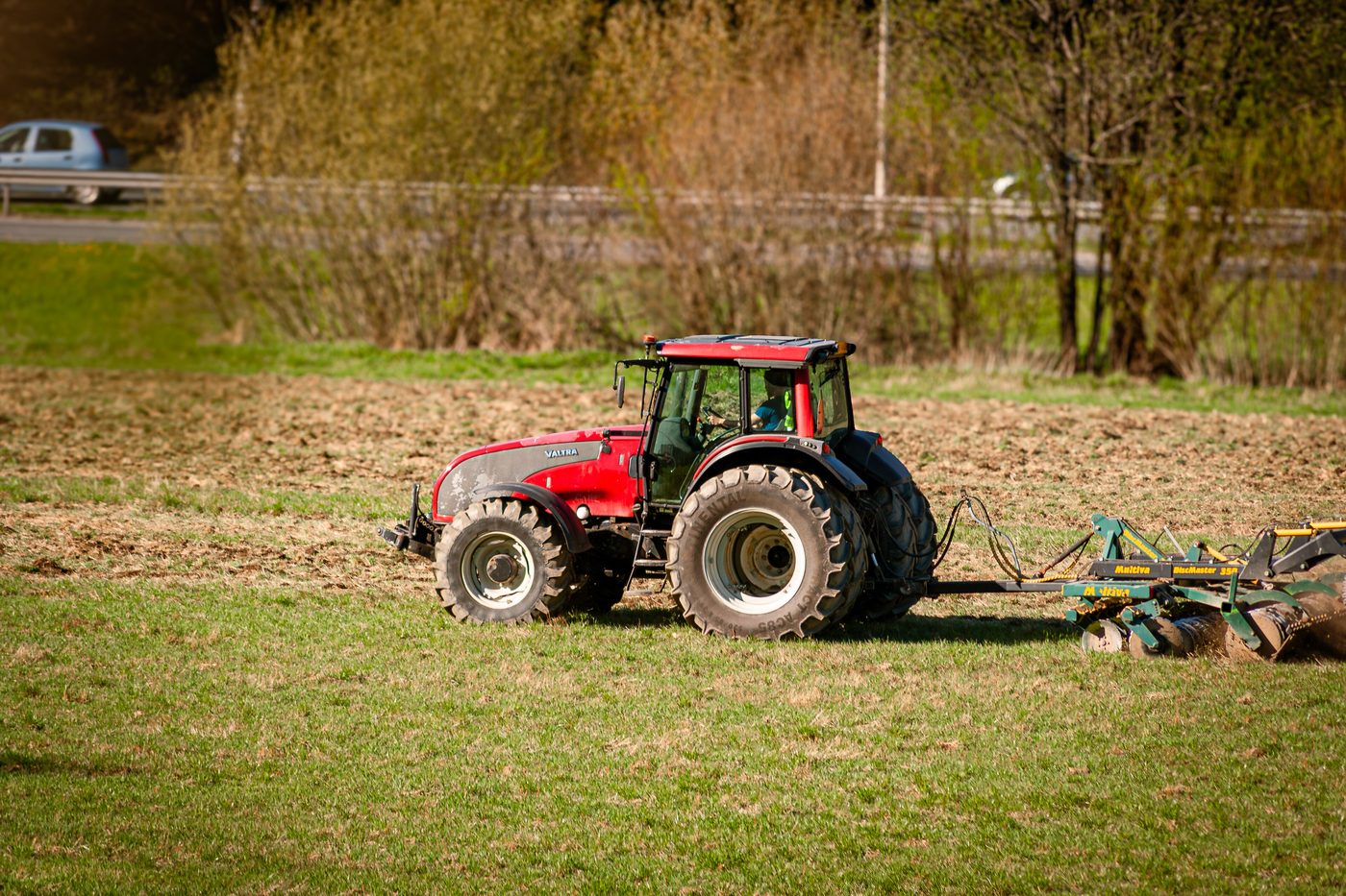 Un tracteur rouge tirant une herse dans un champ